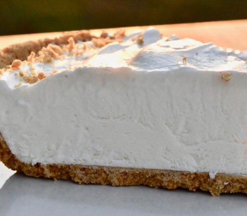 A close-up of a slice of creamy pie with a graham cracker crust, showcasing its smooth, white filling.