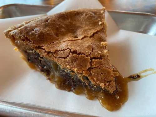 A slice of dessert with a cracked, golden-brown top and a gooey, chocolatey filling oozing out.