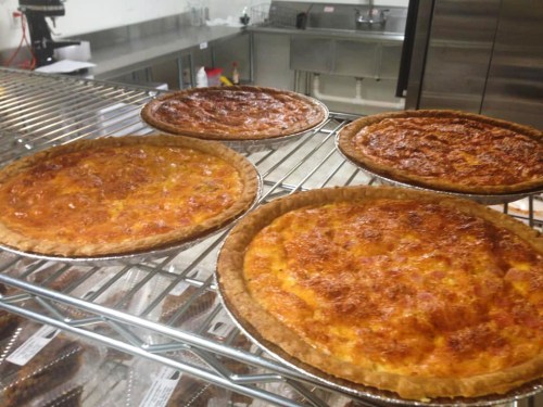 Four freshly baked pies cooling on a wire rack in a kitchen.