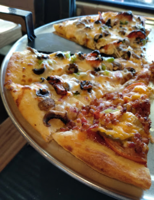 A close-up of a pizza on a metal tray, topped with cheese, pepperoni, olives, and various vegetables.