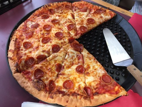 A large pepperoni pizza with several slices cut, resting on a black pizza tray with a metal pizza cutter.