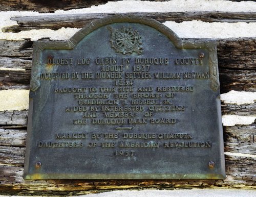 Plaque detailing the history of the oldest log cabin in Dubuque County, established in 1827 and restored in 1937.