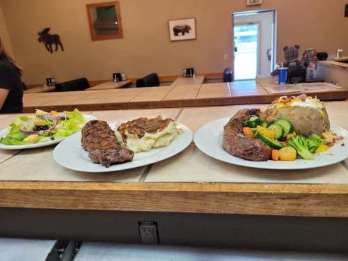 Three plates of food: two steaks with sides of mashed potatoes and vegetables, and a salad on the left.