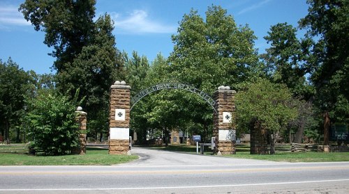 Stone entrance gate with archway surrounded by trees and greenery, leading to a park or historical site.