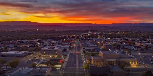 Aerial view of a town at sunset, with vibrant colors in the sky and city lights beginning to glow.