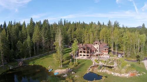 Aerial view of a large house surrounded by lush green trees and a serene pond in a forested area.