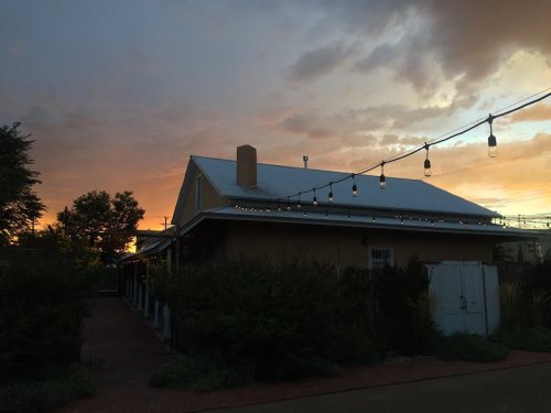 A cozy house at sunset, with string lights and a colorful sky in the background.