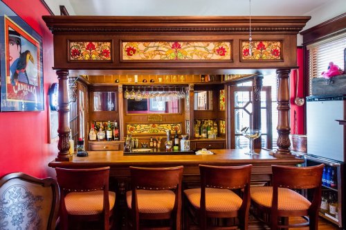 A wooden bar with stained glass details, surrounded by high chairs, in a cozy, warmly lit room.