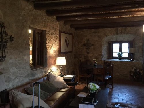 Cozy rustic interior with stone walls, wooden beams, a sofa, and a small dining area by a window.