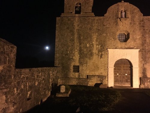 A historic stone church at night, illuminated by moonlight, with a clear sky and a visible moon in the background.