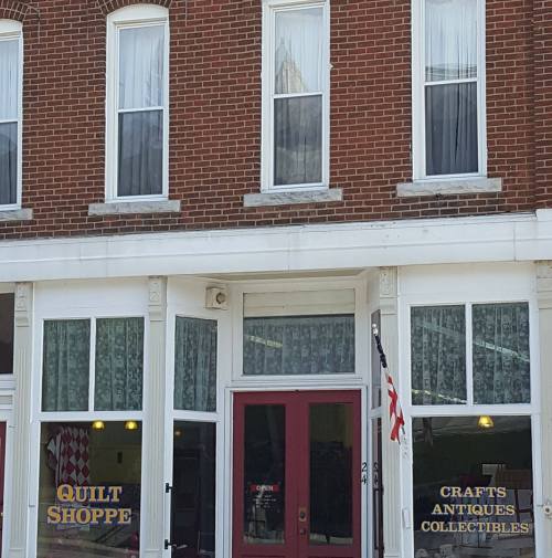 A brick storefront featuring two shops: "Quilt Shoppe" and "Craft's Antiques & Collectibles," with large windows.