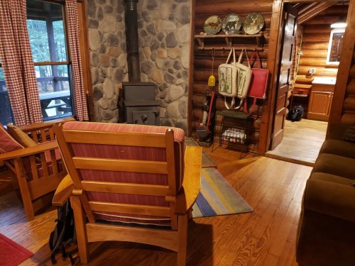 Cozy log cabin interior with wooden furniture, a stone fireplace, and a view of the kitchen area.