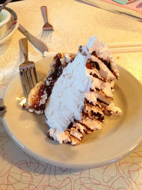 A slice of layered cake with frosting and filling, served on a plate with a fork beside it.