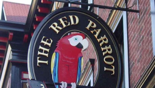 Sign featuring a colorful parrot with the text "The Red Parrot" on a black circular background.