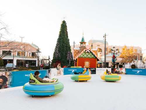 People enjoying bumper cars on ice, surrounded by festive decorations and a large Christmas tree.