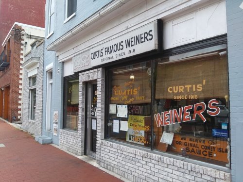 Exterior of Curtis' Famous Weiners, a historic eatery with large windows displaying the menu and "OPEN" sign.