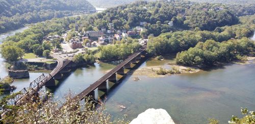 Aerial view of a small town surrounded by greenery, with a river and a railway bridge crossing over it.