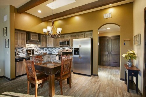 A modern kitchen with wooden beams, stainless steel appliances, and a dining table with chairs. Bright and inviting space.