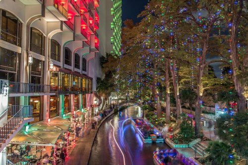 A vibrant night scene along a canal, with colorful lights reflecting on the water and festive decorations in the trees.