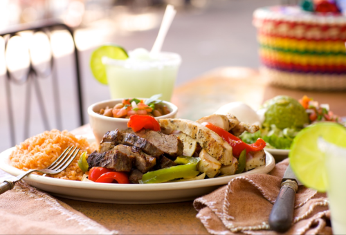 A colorful plate of grilled chicken and steak with rice, beans, guacamole, and a refreshing drink on the side.