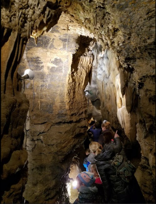 A group of people exploring a narrow cave with rocky walls and dim lighting.