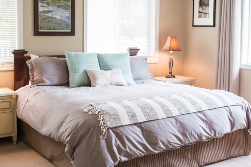 Cozy bedroom featuring a large bed with gray bedding, decorative pillows, and soft lighting from a bedside lamp.