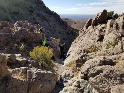 Hikers navigating rocky terrain in a mountainous landscape under a clear sky.