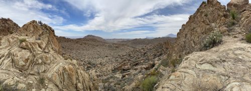A panoramic view of a rocky desert landscape under a cloudy sky, with distant mountains in the background.