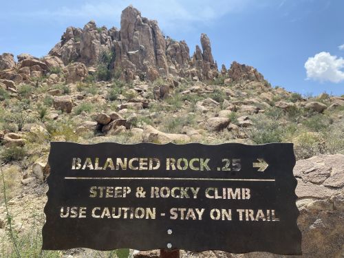 Sign directing hikers to Balanced Rock, warning of a steep and rocky climb ahead. Scenic rocky landscape in the background.