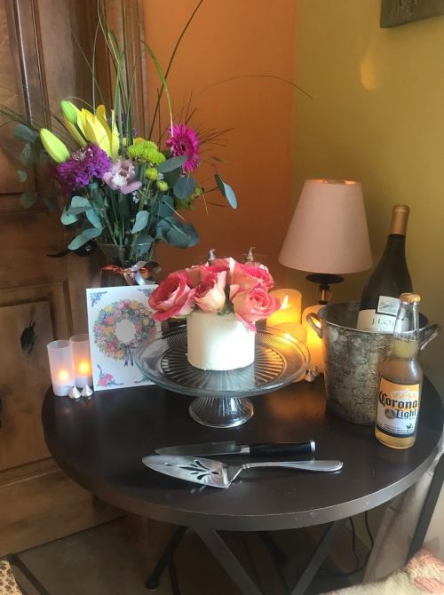 A cozy table setting with a cake, flowers, candles, a bottle of champagne, and a beer, creating a festive atmosphere.