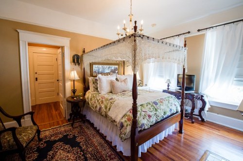 Cozy bedroom featuring a four-poster bed, floral bedding, a vintage chair, and warm wooden accents.