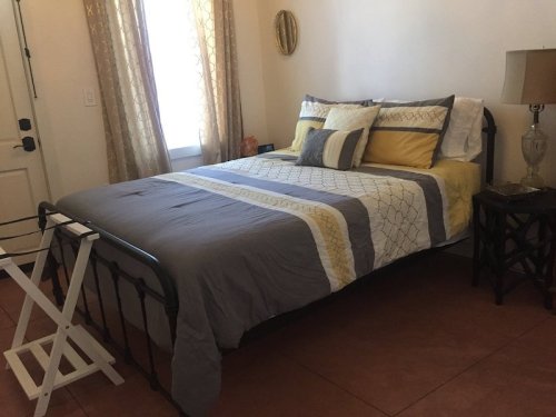 A cozy bedroom featuring a bed with gray and yellow bedding, a lamp, and a folding chair beside it.