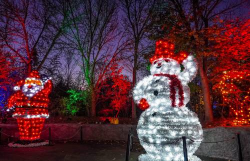 Colorful holiday lights illuminate a snowman and Santa Claus in a festive outdoor setting at dusk.