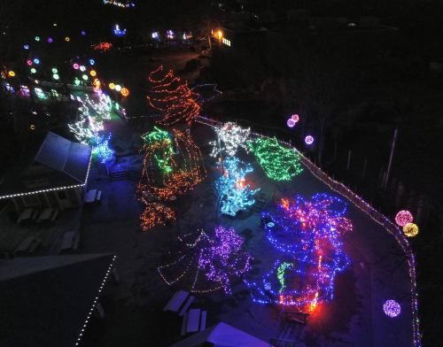 Aerial view of a festive display with colorful Christmas lights on trees and decorations in a dark setting.