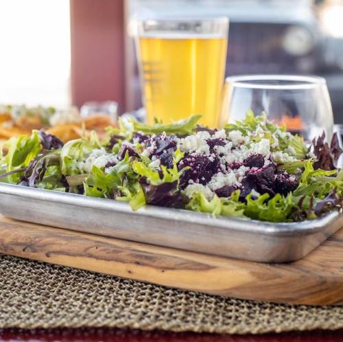 A fresh salad with mixed greens and feta cheese, served on a wooden platter with a glass of beer in the background.