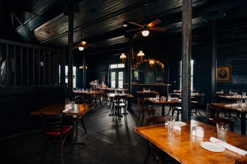 A dimly lit restaurant interior with wooden tables, chairs, and ceiling fans, featuring a rustic ambiance.