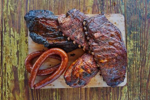 A wooden board featuring a variety of smoked meats, including ribs, brisket, and sausage, with a rustic background.