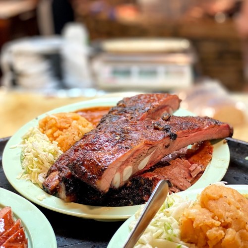 Plates of grilled meat with sides of rice and cabbage, served in a vibrant, casual dining setting.