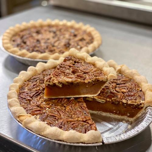 Two pecan pies, one partially sliced, showcasing a golden filling and a flaky crust, on a silver surface.