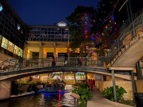 A scenic view of a lit-up canal at night, featuring a bridge, shops, and a boat on the water.