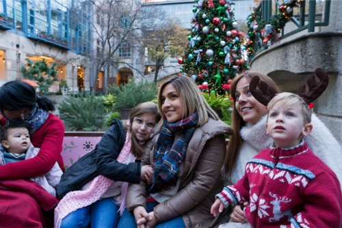 A family sits together in front of a decorated Christmas tree, smiling and enjoying the holiday spirit.