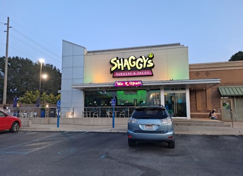 Exterior of Shaggy's Burgers & Tacos at dusk, featuring a colorful sign and a parked car in the foreground.