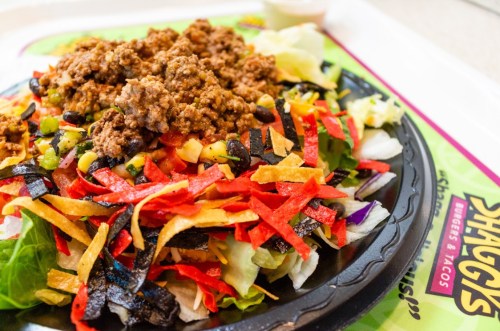 A colorful salad topped with seasoned beef, black beans, and crispy tortilla strips on a tray.