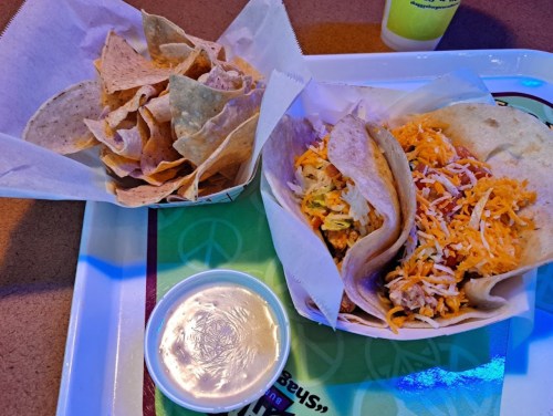 A tray with two soft tacos filled with cheese and chicken, alongside a bowl of salsa and a serving of tortilla chips.
