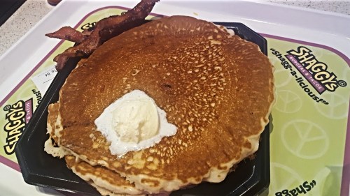A plate of fluffy pancakes topped with butter and served with crispy bacon on the side.
