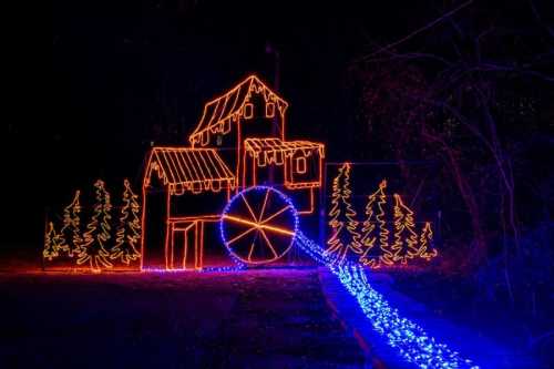 A colorful display of lights depicting a house with a water wheel and surrounding trees, set against a dark background.