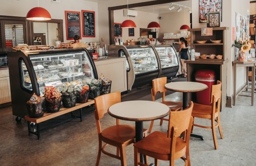 A cozy café interior with display cases, tables, and chairs, featuring baked goods and a welcoming atmosphere.