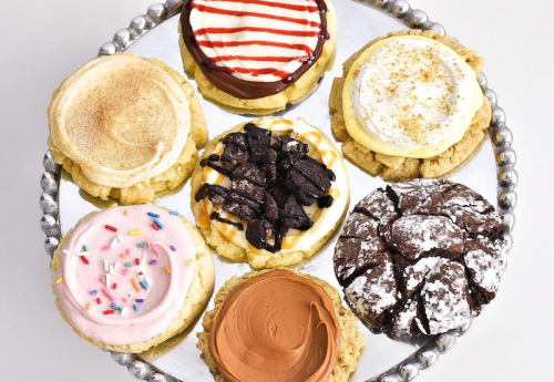 A silver platter holds eight colorful cookies with various frostings and toppings, including sprinkles and chocolate.