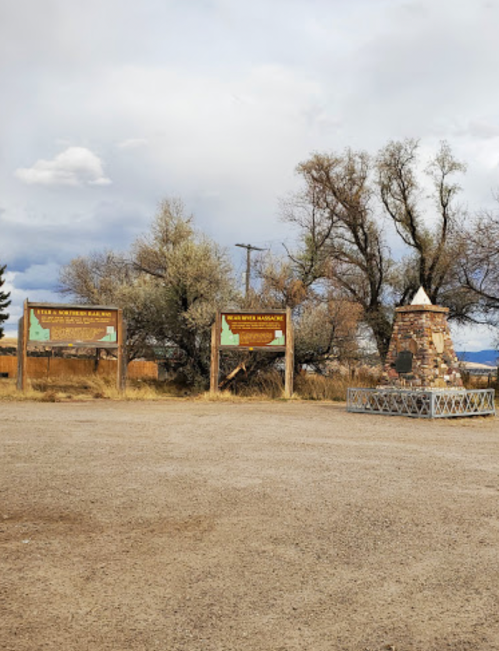 Two informational signs about the Bear River Massacre, with a stone monument nearby, set in a rural landscape.