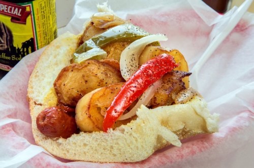 A sandwich filled with grilled chicken, peppers, and onions on a soft roll, served with a side drink.